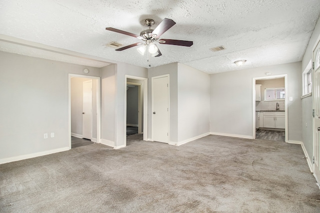 unfurnished bedroom with a textured ceiling, ceiling fan, ensuite bath, and carpet floors