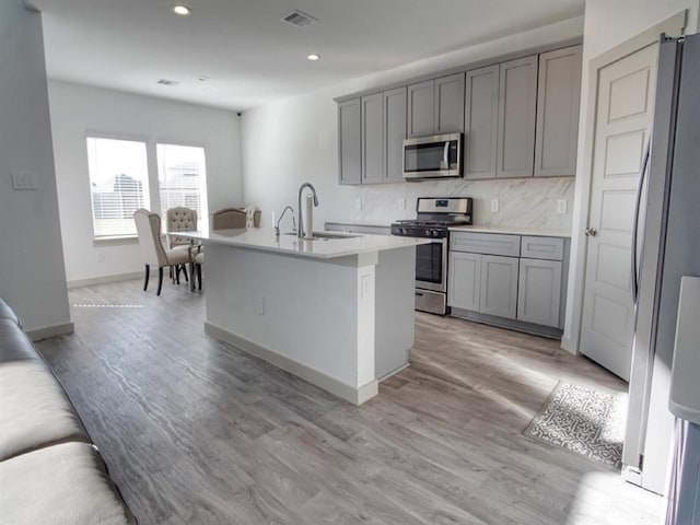 kitchen featuring a kitchen island with sink, gray cabinets, sink, appliances with stainless steel finishes, and light hardwood / wood-style floors