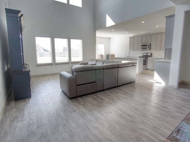 living room featuring a high ceiling, sink, and light hardwood / wood-style flooring