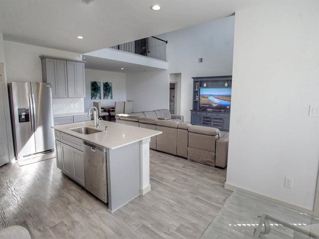 kitchen with light wood-type flooring, stainless steel appliances, an island with sink, sink, and gray cabinetry