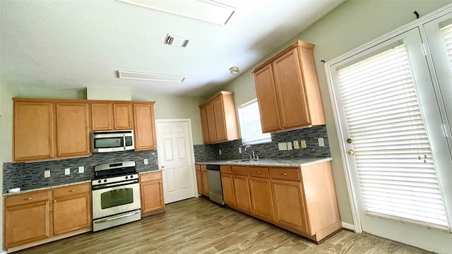 kitchen with backsplash, stainless steel appliances, light stone counters, sink, and light hardwood / wood-style floors