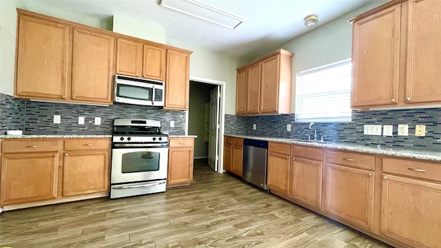 kitchen featuring stainless steel appliances, sink, tasteful backsplash, and light hardwood / wood-style flooring