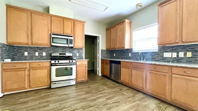 kitchen featuring light hardwood / wood-style flooring, backsplash, sink, light stone countertops, and appliances with stainless steel finishes