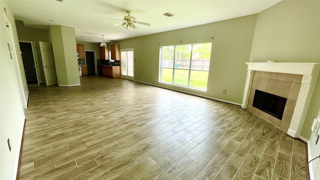 unfurnished living room featuring ceiling fan, a tile fireplace, and light hardwood / wood-style floors