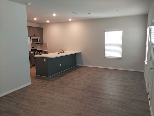 kitchen with appliances with stainless steel finishes, dark hardwood / wood-style flooring, kitchen peninsula, and sink