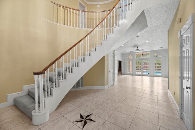 staircase featuring french doors, tile patterned flooring, a textured ceiling, a towering ceiling, and ceiling fan