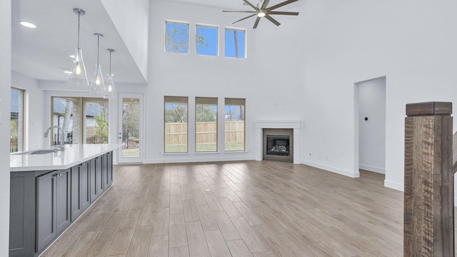 unfurnished living room with a ceiling fan, baseboards, a fireplace, a sink, and light wood-type flooring