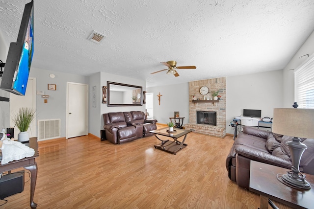 living room featuring a textured ceiling, hardwood / wood-style floors, ceiling fan, and a large fireplace