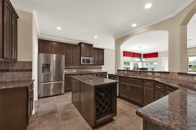 kitchen with stainless steel appliances, sink, decorative light fixtures, dark stone countertops, and a center island