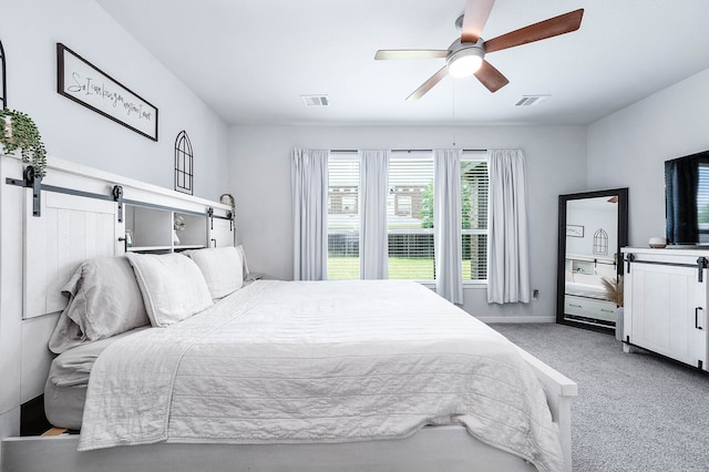 bedroom featuring light colored carpet, ceiling fan, and a barn door