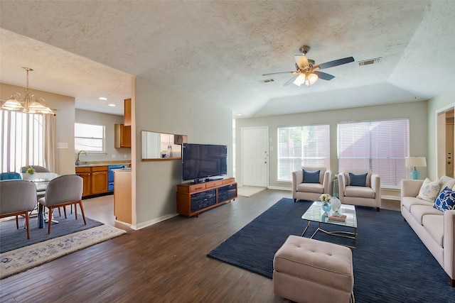 living room with ceiling fan with notable chandelier, a wealth of natural light, dark hardwood / wood-style floors, and a textured ceiling