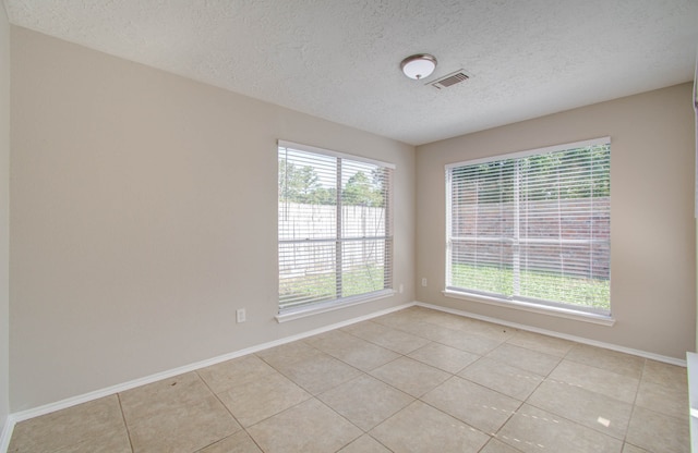 unfurnished room with a textured ceiling, a wealth of natural light, and light tile patterned floors