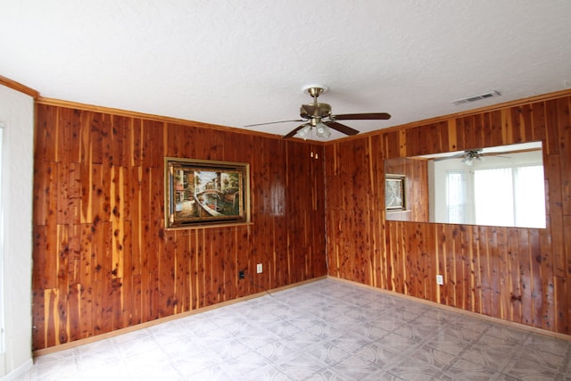 spare room featuring ornamental molding, a textured ceiling, ceiling fan, and wooden walls