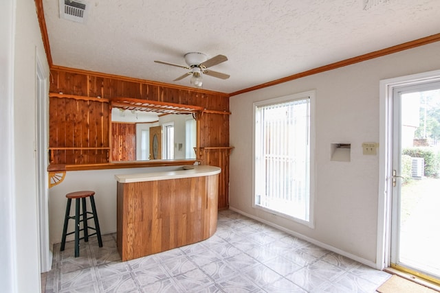 kitchen with kitchen peninsula, wood walls, ceiling fan, ornamental molding, and a textured ceiling