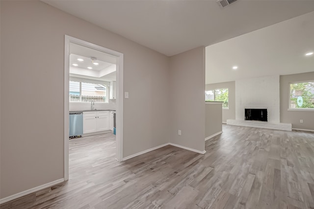 unfurnished living room featuring a raised ceiling, sink, a brick fireplace, and light hardwood / wood-style floors