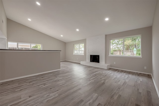 unfurnished living room with a fireplace, lofted ceiling, plenty of natural light, and light hardwood / wood-style floors