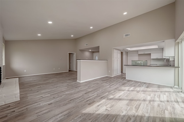 unfurnished living room with light wood-type flooring, high vaulted ceiling, a fireplace, and sink