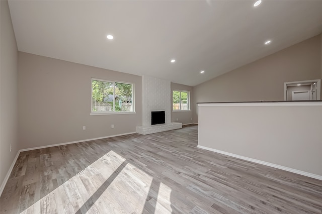 unfurnished living room with lofted ceiling, a fireplace, and light wood-type flooring