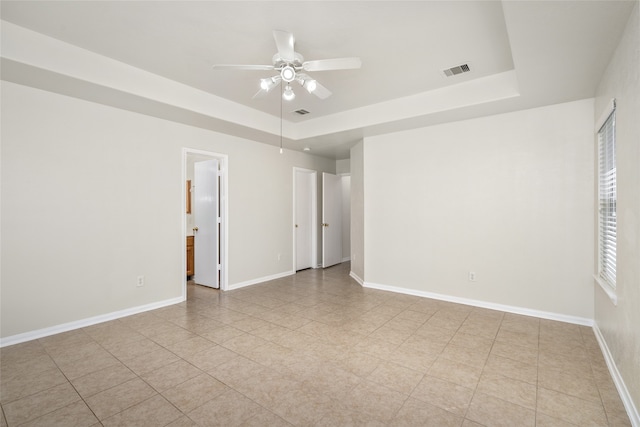 unfurnished room with ceiling fan, light tile patterned floors, and a raised ceiling