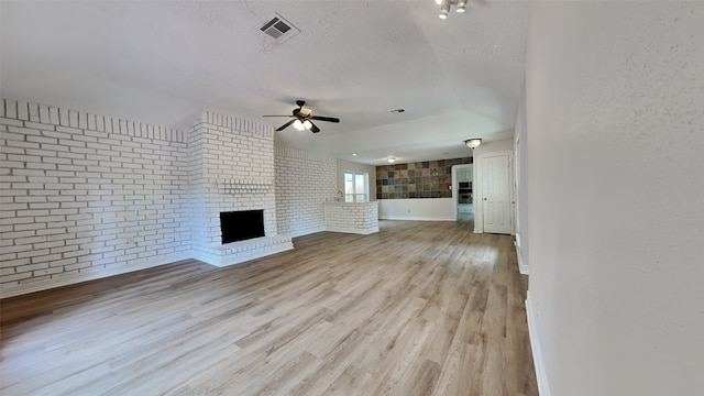 unfurnished living room with light hardwood / wood-style floors, a textured ceiling, a brick fireplace, ceiling fan, and brick wall