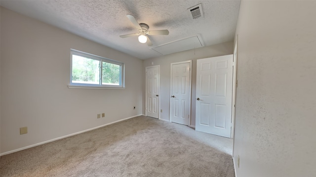 unfurnished bedroom with two closets, ceiling fan, light colored carpet, and a textured ceiling