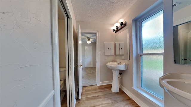 bathroom with wood-type flooring, a textured ceiling, toilet, and ceiling fan