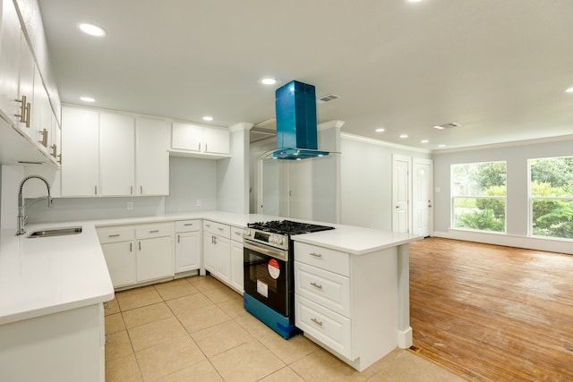 kitchen with light wood-type flooring, white cabinetry, exhaust hood, sink, and gas range