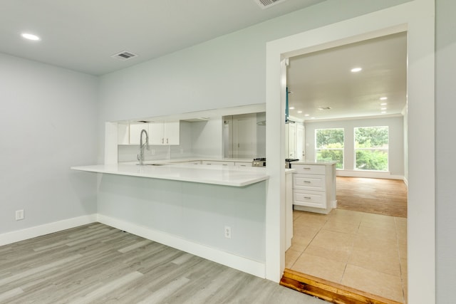 kitchen with kitchen peninsula, sink, white cabinetry, and light hardwood / wood-style floors