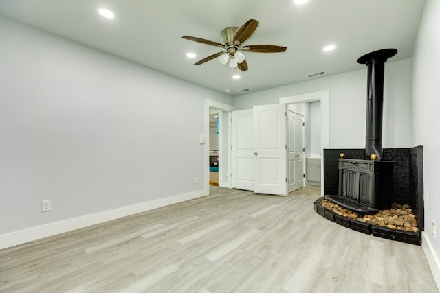 unfurnished living room featuring a wood stove, ceiling fan, and light wood-type flooring