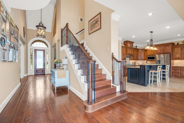 entrance foyer with crown molding, dark wood-type flooring, an inviting chandelier, and a towering ceiling