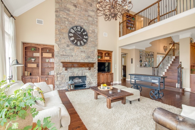 living room with hardwood / wood-style floors, a towering ceiling, a stone fireplace, ornamental molding, and a chandelier