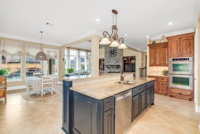 kitchen featuring pendant lighting, appliances with stainless steel finishes, an island with sink, light stone counters, and a chandelier