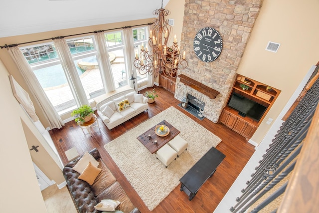 living room with a high ceiling, a stone fireplace, an inviting chandelier, and hardwood / wood-style floors