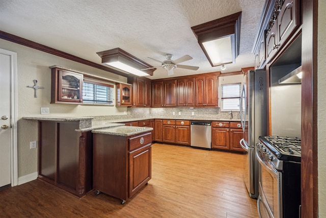 kitchen with a textured ceiling, light hardwood / wood-style flooring, stainless steel appliances, ornamental molding, and ceiling fan