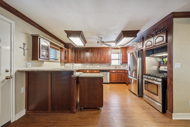 kitchen with light hardwood / wood-style flooring, appliances with stainless steel finishes, crown molding, kitchen peninsula, and ceiling fan