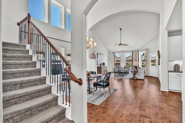 stairs with high vaulted ceiling, ceiling fan with notable chandelier, and hardwood / wood-style floors