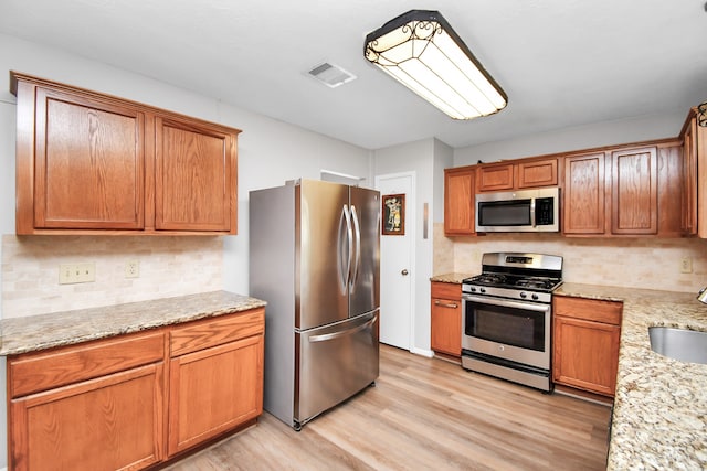 kitchen featuring appliances with stainless steel finishes, decorative backsplash, light hardwood / wood-style floors, light stone counters, and sink