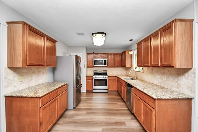 kitchen featuring hanging light fixtures, light hardwood / wood-style floors, stainless steel appliances, and light stone counters