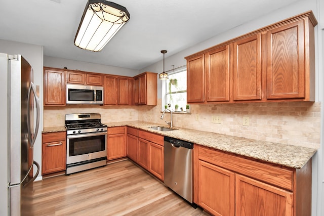 kitchen with appliances with stainless steel finishes, light stone countertops, light wood-type flooring, decorative light fixtures, and sink