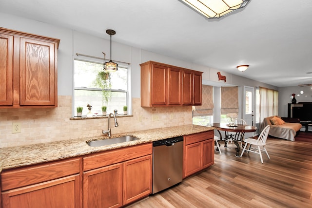 kitchen featuring light stone countertops, sink, stainless steel dishwasher, decorative light fixtures, and light wood-type flooring