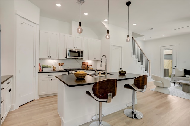 kitchen with appliances with stainless steel finishes, sink, light wood-type flooring, decorative light fixtures, and a kitchen island with sink