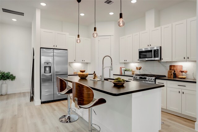 kitchen featuring white cabinets, a kitchen island with sink, light hardwood / wood-style flooring, pendant lighting, and stainless steel appliances