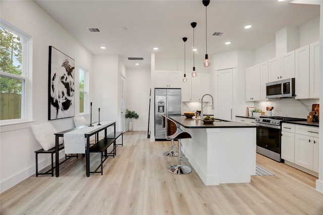 kitchen with a breakfast bar area, appliances with stainless steel finishes, a kitchen island with sink, pendant lighting, and sink