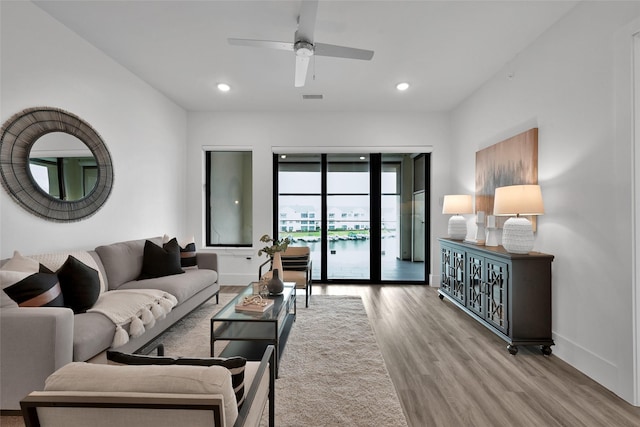 living room featuring ceiling fan, a water view, and light wood-type flooring