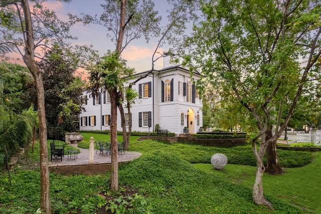 property exterior at dusk with a lawn and a patio