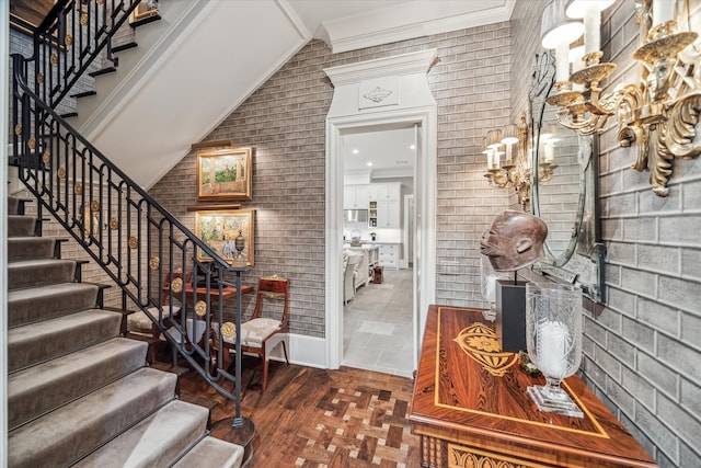 entrance foyer featuring lofted ceiling, crown molding, and brick wall