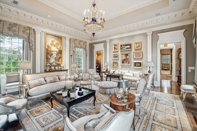 living room with an inviting chandelier, hardwood / wood-style floors, a tray ceiling, decorative columns, and ornamental molding