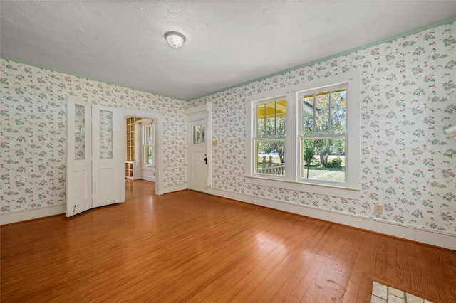 empty room with wallpapered walls, light wood-style floors, baseboards, and a textured ceiling