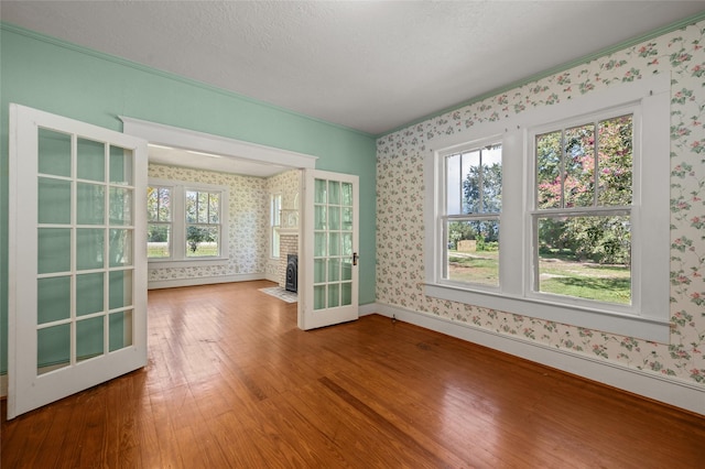 empty room with baseboards, wood-type flooring, a textured ceiling, and wallpapered walls