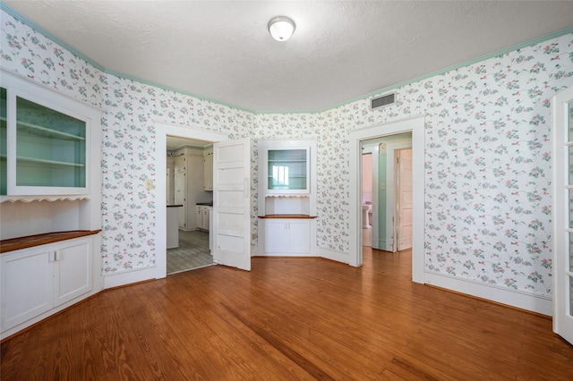 interior space with wallpapered walls, wood finished floors, visible vents, and a textured ceiling